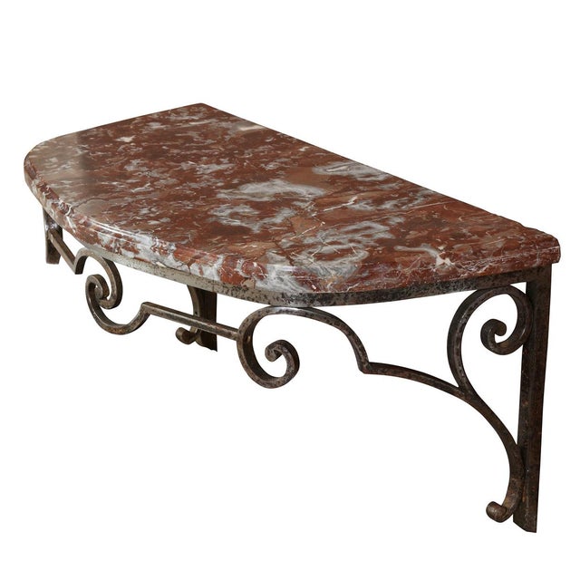 Elegant wall‑mounted demilune console featuring a rich rouge marble top and a sculpted metal base with refined scroll...