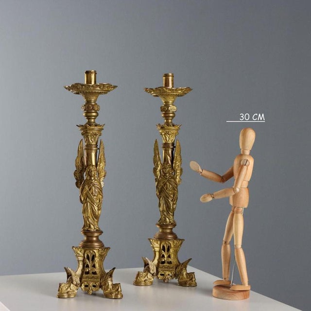 A pair of gilded bronze torch holders supported by three legs shaped like winged animals. In the center is an angel with...
