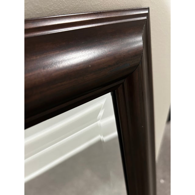 A rectangular wall mirror with a warm, dark mahogany-style wood frame, clean simple molding, and a beveled mirror center....