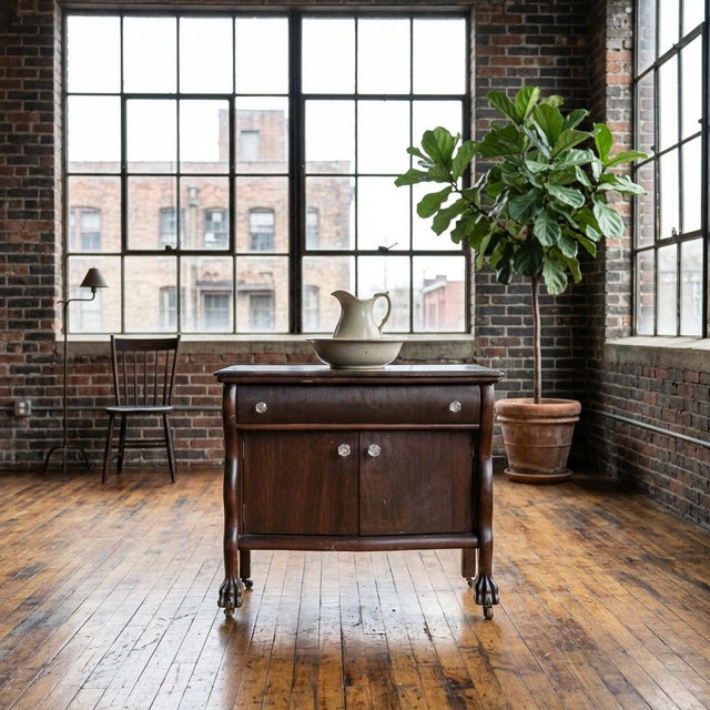 This compact antique cabinet reflects the late American Empire Revival style, with a bowed front and rich dark-stained...