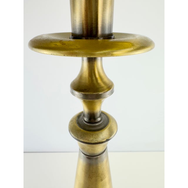 A vintage table lamp featuring a sculptural candlestick-form metal base with a warm antique brass finish and contrasting...