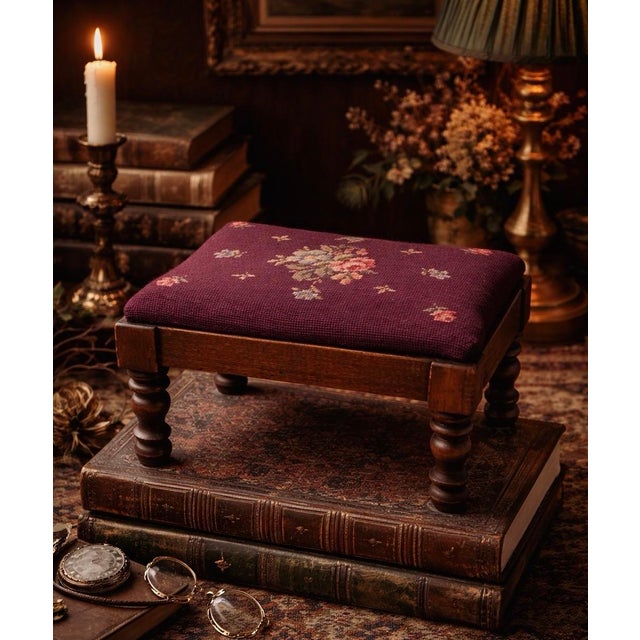 A charming vintage French Provincial footstool featuring hand-worked burgundy wool needlepoint upholstery with a delicate...