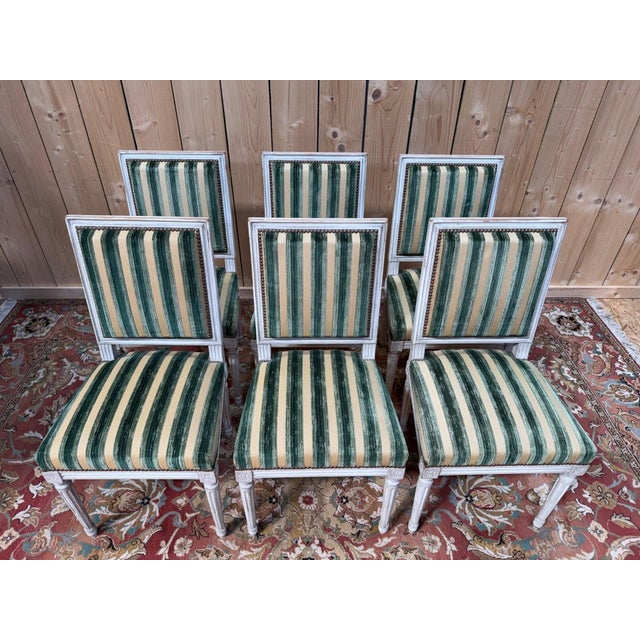A set of six louis xvi style chairs in carved wood, painted a slightly grayish white, displaying a soft and harmonious...