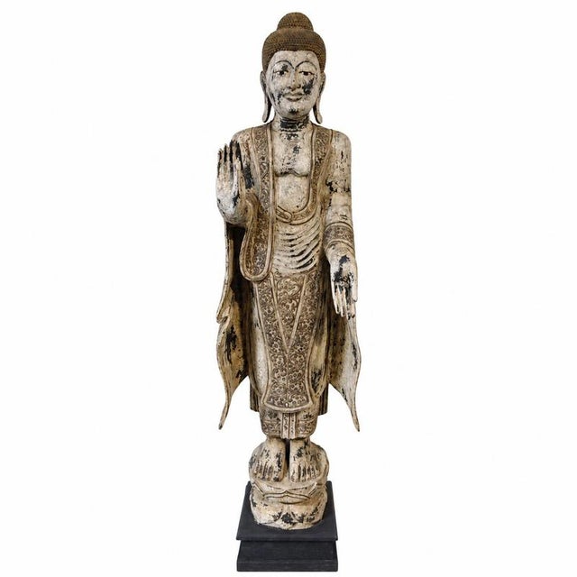 Imposing standing Buddha sculpture, crafted from solid carved wood and set upon a black-painted wooden display base. The...