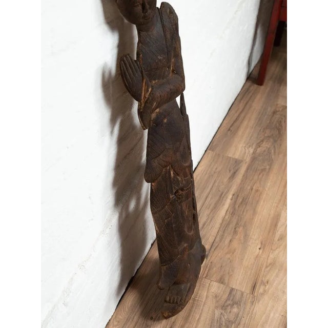 A carved Thai wooden sculpture of a praying Apsara, with flat back and dark patina. Attracting our attention with its dark...