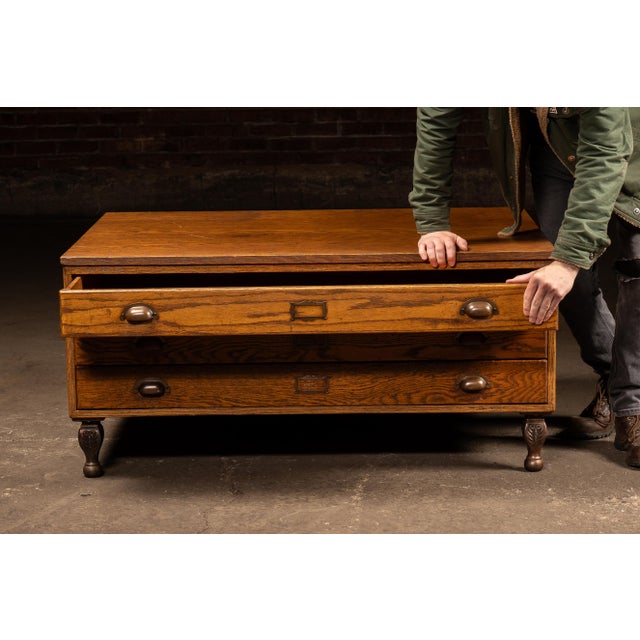 Low-profile oak flat file cabinet featuring a wide rectangular top over two full-width shallow drawers, originally...
