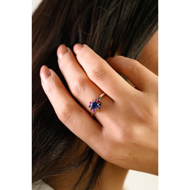 This delicate floral cluster ring features a vibrant round blue sapphire at the center, surrounded by charming halo of...