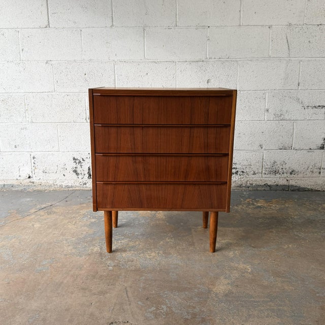 A Danish teak chest from the 1960s with four wide drawers, slim integrated pulls, and tapered legs. The front is kept...