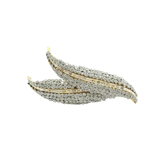 A striking brooch crafted with precision, featuring a dual feather design encrusted with baguette and round brilliant-cut...