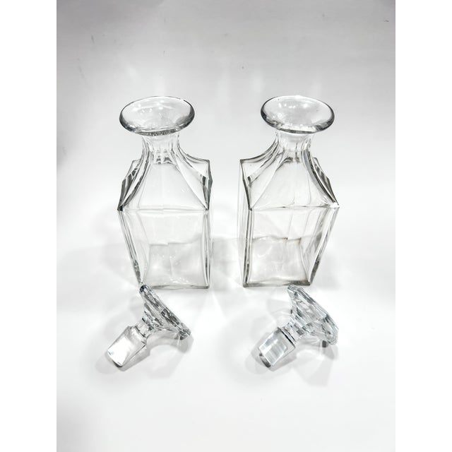 Pair of fine clear crystal decanters. Featuring a minimalist design, each decanter boasts a structured square base with...