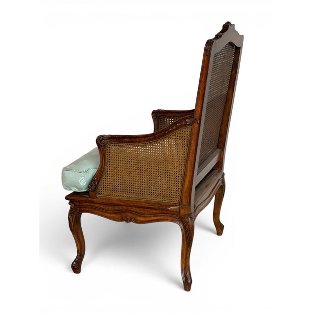 This is a Louis XV style caned bergère chair featuring a carved walnut frame with gracefully scrolled arms, flowing...