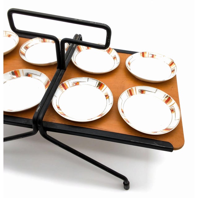 Cool mid century black iron and wood tabletop rack holding a set of eight small white porcelain plates with an orange and...