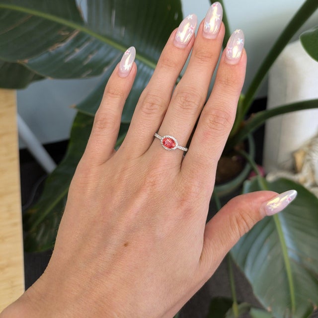 A rare padparadscha sapphire glows in its signature lotus blend of pink and orange at the heart of this oval ring, framed...