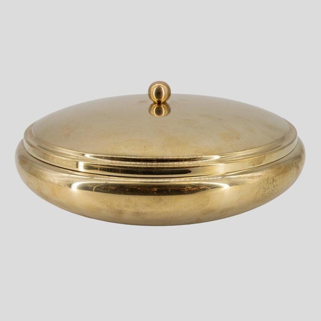A vintage brass bowl with a lid. It has a circular, rounded edges , The lid is slightly domed and features a small...