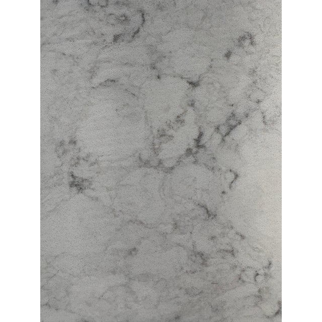 Polished dining table made of marbled quartz has a white marble-patterned top with grey veining. The rectangular surface...