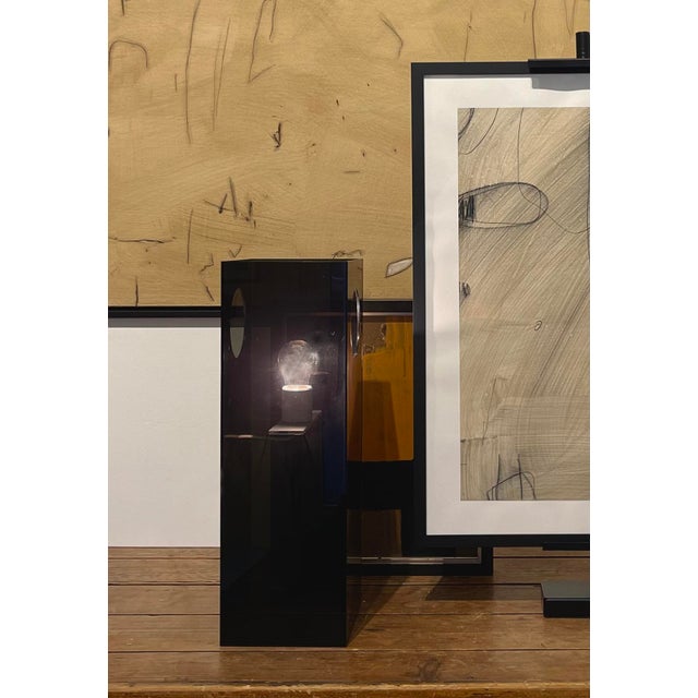 A striking architectural table lamp in smoked acrylic, defined by its clean, monolithic block form and subtle...