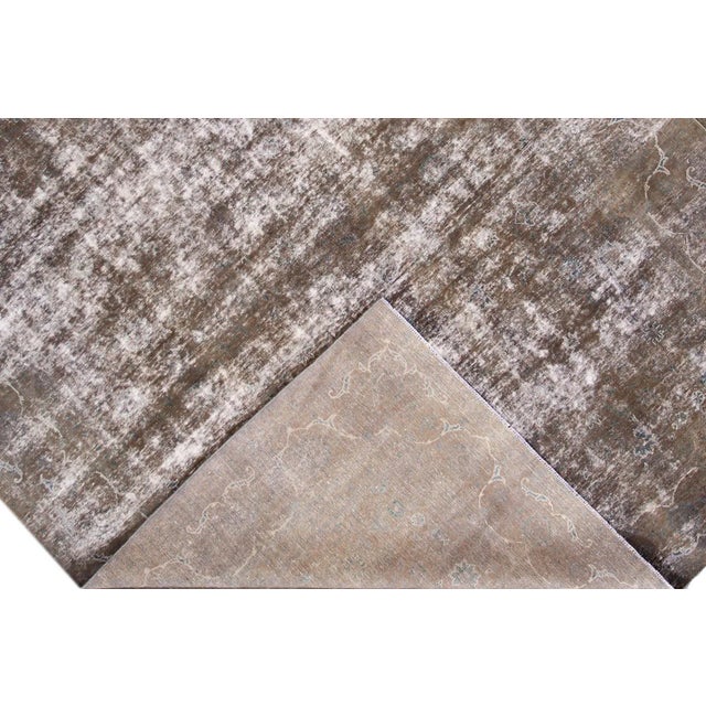 A mid-20th century vintage distressed Persian area rug with a taupe field and subtle all-over floral design. This hand...