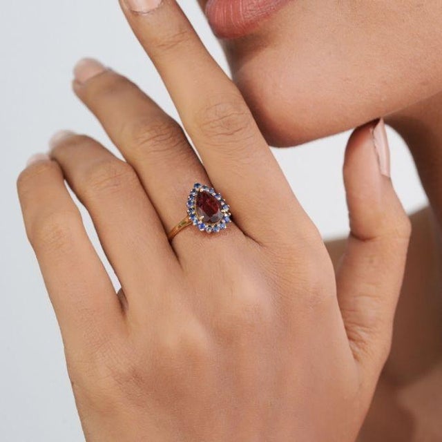 This Retro-style ring featuring a 1.77 carat Rubelite and blue sapphire, set in 18K yellow gold. The pear shape center...