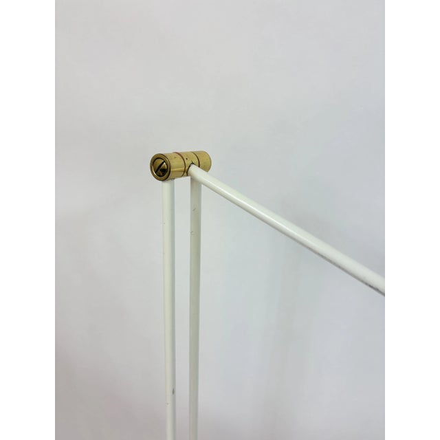 Sleek, minimalist floor lamp with a white metal frame, an elongated round shade, and brass accents at the hinges. European...