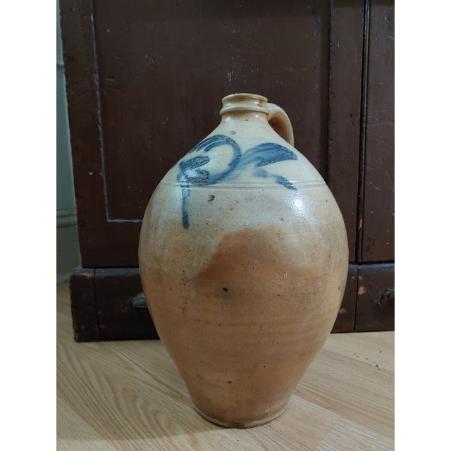 Here's a primitive ovoid shaped stoneware jug circa Mid 19th Century. It features a blue slip design that resembles an...
