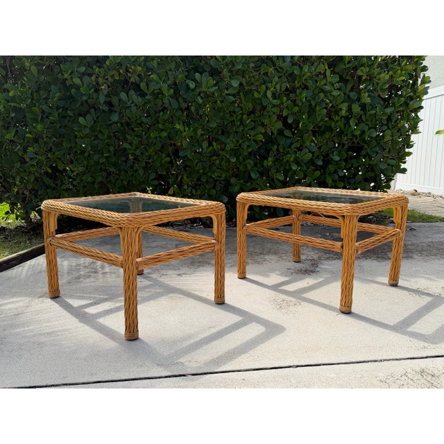 Vintage pair of woven rattan end tables with rectangular glass tops. The tables feature substantial hand-woven rattan...