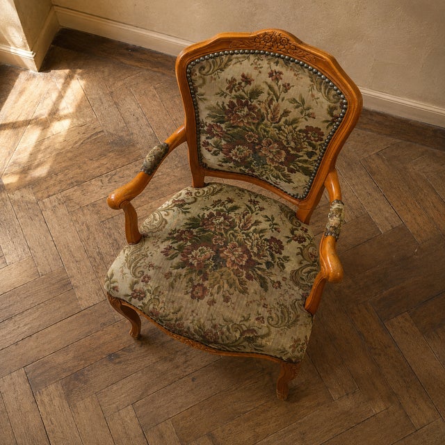 A Louis XV style armchair with a carved wooden frame, shaped armrests, cabriole legs, and floral tapestry upholstery....