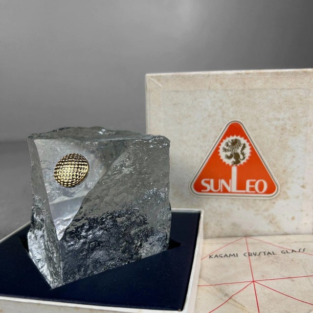 Crystal “ice-glass” block with a clear polished window featuring a gold-colored metal golf ball resting on the surface....