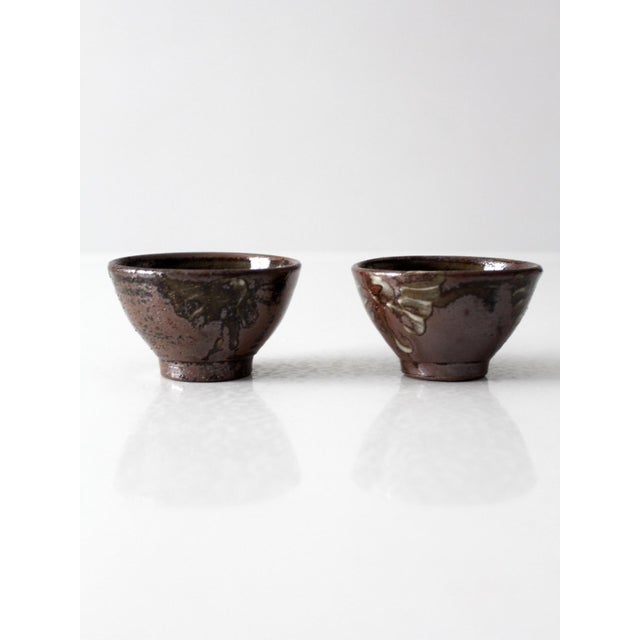 A pair of vintage handmade studio pottery bowls with hand-painted floral decoration in olive and cream over a rich iron-...