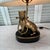 Table lamp with brass bulldog figure mounted on black base. The bulldog holds a bar with picture frame in his mouth. Lamp...