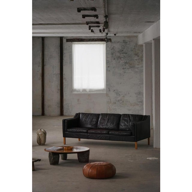 A classic Danish Modern three-seater sofa upholstered in patinated black leather, resting on legs crafted from solid...