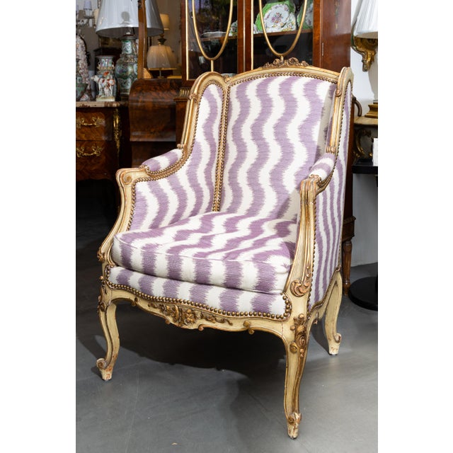 This is a pair of painted and parcel gilt French Louis XV style wing back bergères, upholstered in a quirky contemporary...
