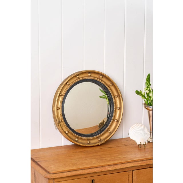 This 19th-century convex gilt mirror features a circular frame with a rich gold-leaf finish and a convex mirror plate....