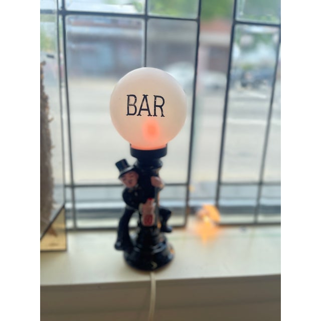 This playful mid-century novelty bar lamp features a glossy black ceramic base molded into the figure of a tipsy man in a...