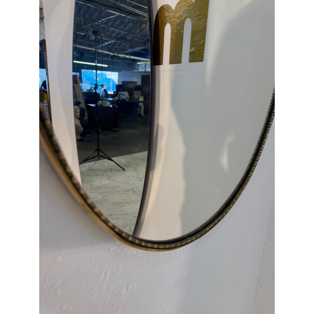 Elegant vintage wall mirror featuring a distinctive shield-inspired silhouette with a sculptural brass frame and...