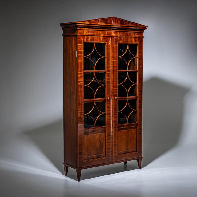 Biedermeier bookcase with two doors, designed as three-quarter glazed panels with diamond-patterned muntins. The case is...