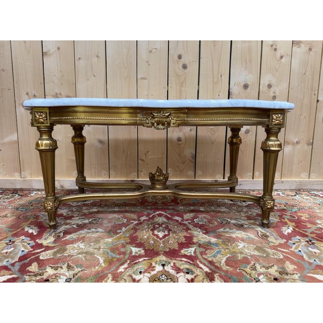 A louis xvi style coffee table in carved wood, regilded with gold paint, with a white carrara marble top veined with gray...