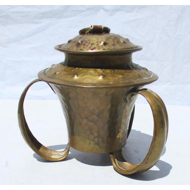Hammered copper 3-handled vessel with large, looping handles that also serve as feet. Fitted lid with ring finial—possibly...