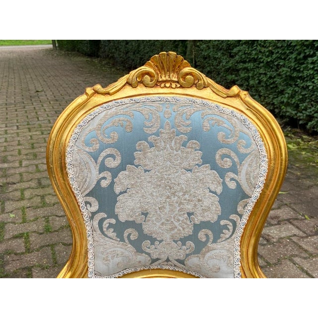 A refined pair of 1950s French Louis XVI-style side chairs, crafted from solid beechwood with a warm gilded finish and...