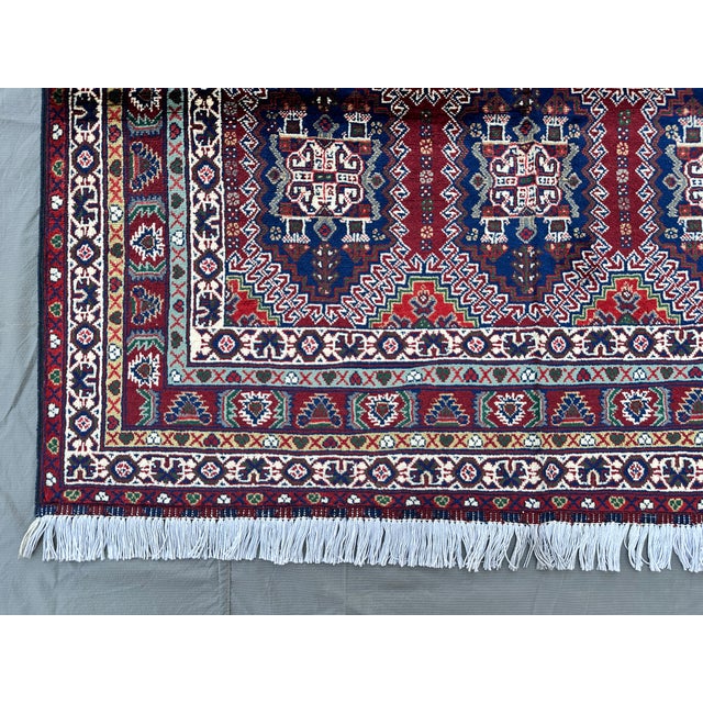 A finely hand-knotted Afghan rug in the classic Caucasian Shirvan style — nine vase-and-blossom panels sit within a bold...