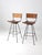 A pair of mid-century Arthur Umanoff style stools featuring black metal frames with woven rush backs and slatted wood...