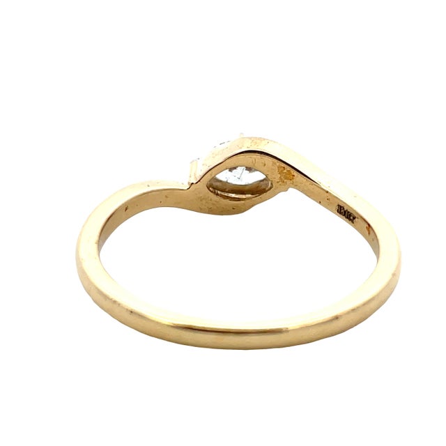 Graceful 18K yellow gold signet-style ring showcasing a marquise diamond in a four-prong setting. The flowing gold...