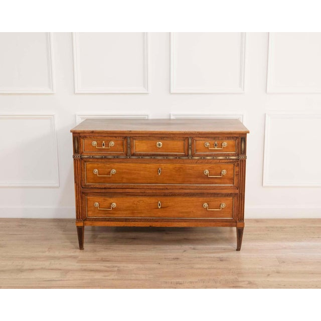A refined Louis XVI walnut chest of drawers opening on the front with five drawers arranged in three rows, exemplifying...