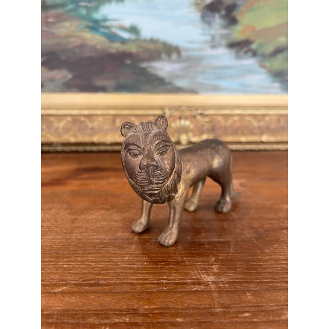 This small bronze toned lion figurine features a possibly hand-cast construction with stylized folk art details, including...