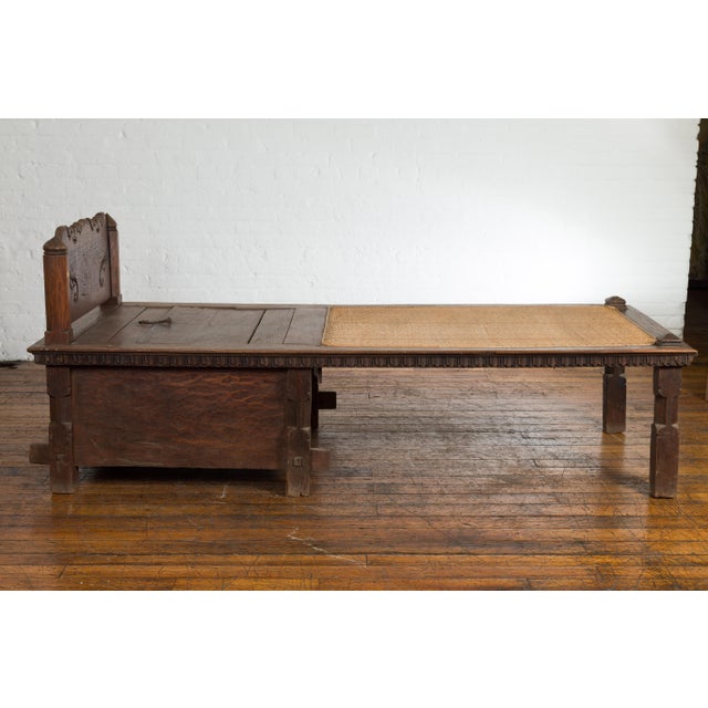An antique Javanese teak wood daybed from the 19th century, with rattan seat, storage and hand carved scrolling motifs....