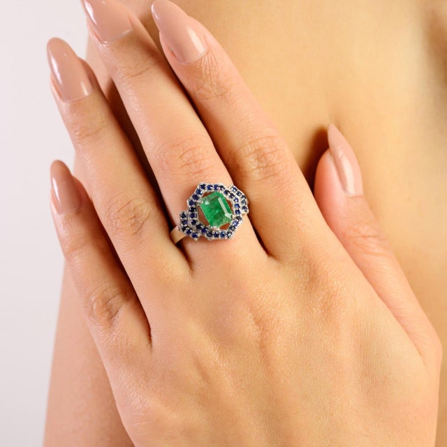 Vintage Art Deco sterling silver ring featuring a striking octagon-cut emerald accented with round blue sapphires. The...