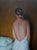 This oil painting captures a figure from behind, draped in a soft white garment that contrasts with the warm yellow and...