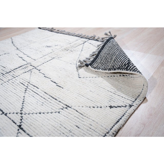A 5' 7" x 8' 7" hand-knotted wool rug with an ivory Berber-style field crossed by irregular charcoal lines, with a lightly...