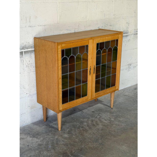 This cabinet features an enclosed silhouette supported by four tapered legs. Two prominent doors showcase multi-colored...