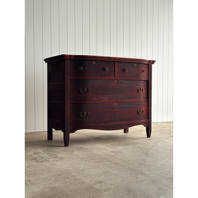 Antique mahogany chest of drawers with a shaped top and broad serpentine front, the surface showing deep oxblood tones...