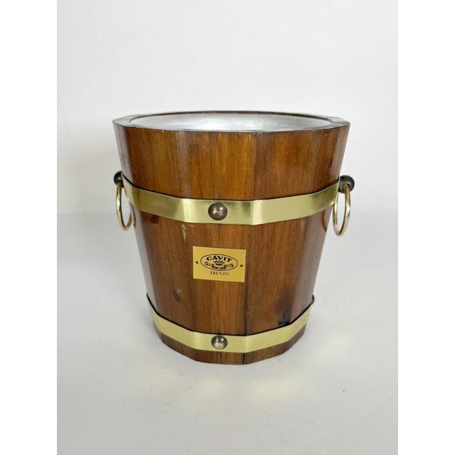 An elegant vintage wooden ice bucket, banded in polished brass and featuring two side handles with metal rings. Its design...